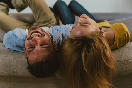 Young couple spending time together at home. Man and woman sitting on the couch and having funの写真素材
