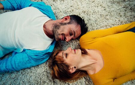 Young couple spending time together at home. Man and woman lying down on the carpet and having fun.