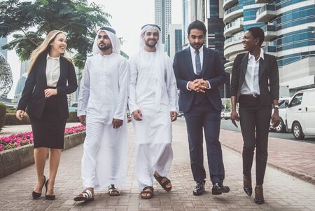 Mixed business team in Dubai. Business meeting with men wearing kandura and western people walking on the streetの写真素材