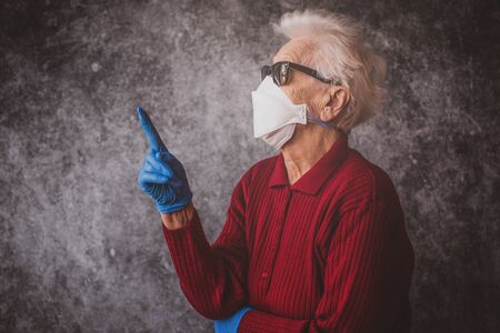 Old grandmother protect herself from coronavirus infection with medical gloves and respirator maskの写真素材