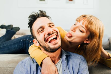 Two young adults at home - happy couple of lovers cuddling on the sofaの写真素材