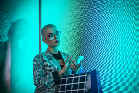 Image of a beautiful young woman posing against a led panel. Shaved head teenager with alternative...