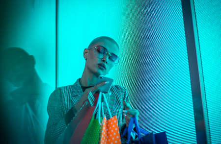 Image of a beautiful young woman posing against a led panel. Shaved head teenager with alternative...