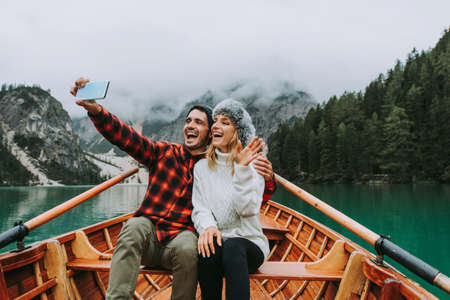 Beautiful couple of young adults visiting an alpine lake at Braies, Italy - Tourists with hiking outfit having fun on vacation during autumn foliage - Concepts about travel, lifestyle and wanderlustの写真素材