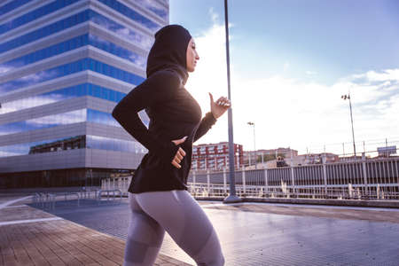 Muslim urban runner training in the city center. Beautiful woman doing sport in the early morning