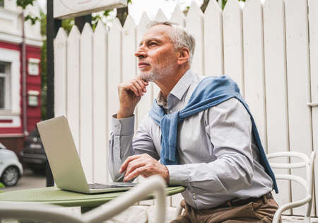 Cheerful senior man portrait - Mature adult using his computer laptop in a bar coffeehouse, concepts about lifestyle, senior people, technology and smart workingの写真素材
