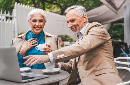Beautiful senior couple dating outdoors - Mature couple with laptop computer sitting in a bar restaurant, concepts about elderly, lifestyle and technologyの写真素材