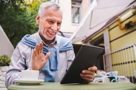 Cheerful senior man portrait - Mature adult using his computer laptop in a bar coffeehouse, concepts...