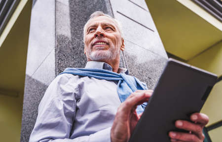 Cheerful senior man portrait - Mature adult using his computer laptop in a bar coffeehouse, concepts...