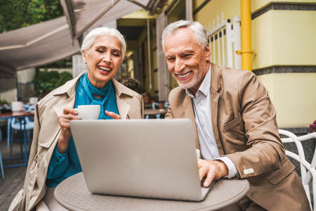 Beautiful senior couple dating outdoors - Mature couple with laptop computer sitting in a bar restaurant, concepts about elderly, lifestyle and technologyの写真素材