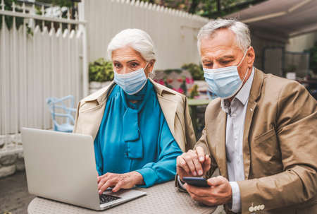 Beautiful senior couple with laptop computer sitting in a bar restaurant, communicating with family on a video call - concepts about elderly, lifestyle, technology and social distancing during corona virus pandemic quarantineの写真素材