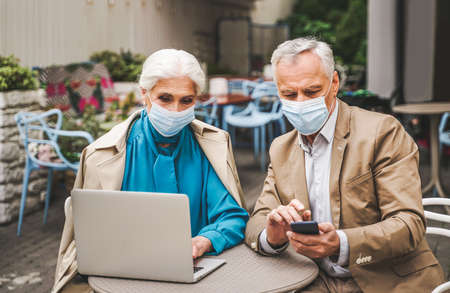 Beautiful senior couple with laptop computer sitting in a bar restaurant, communicating with family on a video call - concepts about elderly, lifestyle, technology and social distancing during corona virus pandemic quarantineの写真素材