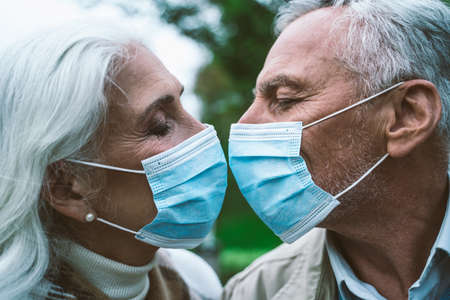 Happy senior couple kissing in the park wearing medical masksの写真素材