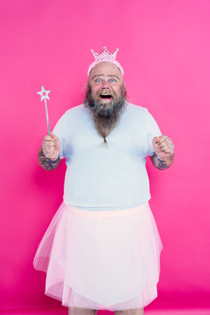 Funny man dancing and having fun wearing a ballet outfit. Happy princess on a pink colored backgroundの写真素材