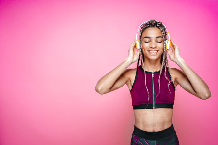 Beautiful girl doing exercises and sport. Posing on a pink colored background while listening some musicの写真素材
