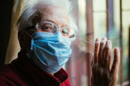 Old woman portrait at the window. Grandmother looking out on the street. "staying at home" and "quarantine" concept about 2020 coronavirus periodの写真素材