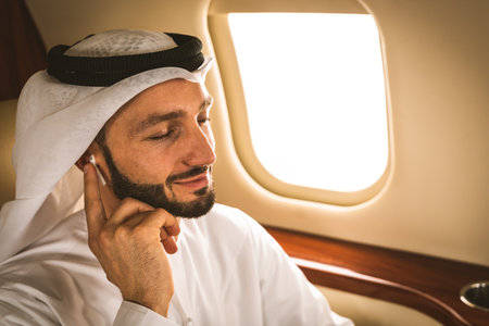 Arabic man wearing kandora in emirates style flying on exclusive private jet - Middle-eastern businessman with traditional dress flies in exclusive business class on airplane, concepts about business and transportationの写真素材
