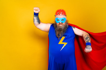 Funny fat man with superhero costume acting as superhuman with special powers, portrait on colored backgroundの写真素材