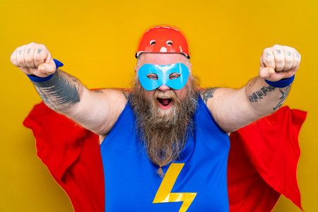 Funny fat man with superhero costume acting as superhuman with special powers, portrait on colored backgroundの写真素材