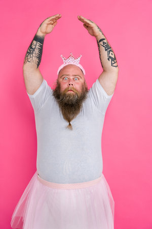 Funny fat man pretending to be a ballerina with tutu - Comic character with beard and tattooes dancing on a pink backgroundの写真素材