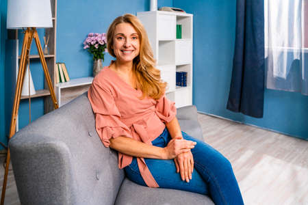 Beautiful adult woman sitting alone at home and looking at camera smilingの写真素材
