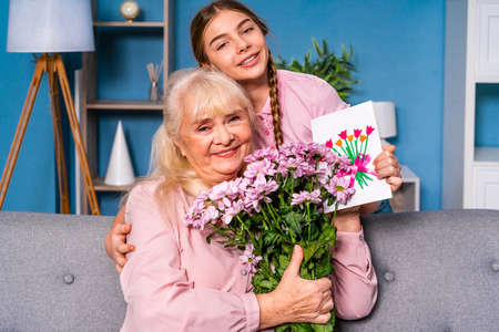 Grandchild presenting flowers to granny at home, happy domestic life moments - Family having fun, concepts about elderly, mult-generation family and relationshipの写真素材