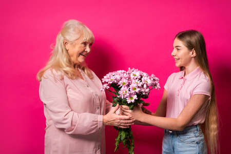 Grandchild presenting flowers to granny at home, happy domestic life moments - Family having fun, concepts about elderly, mult-generation family and relationshipの写真素材