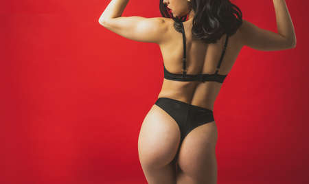 Image of a beautiful woman posing in lingerie on a red colored backgroundの写真素材