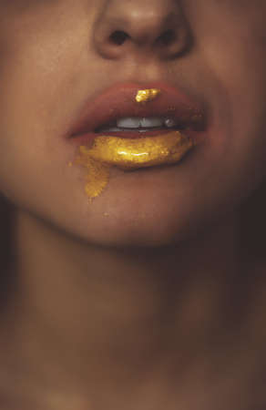 Artistic image of a female mouth with golden fluid dripping on the chinの写真素材
