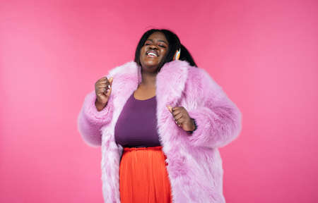Image of a beautiful woman posing in a furry coat on a pink backgroundの写真素材