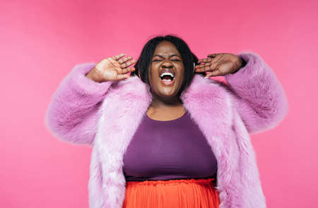 Image of a beautiful woman posing in a furry coat on a pink backgroundの写真素材