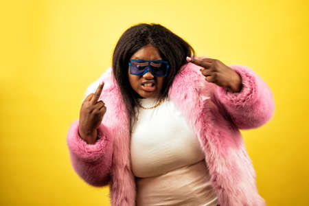 Image of a beautiful woman posing in a furry coat on a yellow backgroundの写真素材