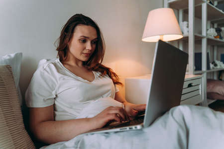 lifestyle moments of a young woman at home. Woman working on the laptop before going to sleepの写真素材