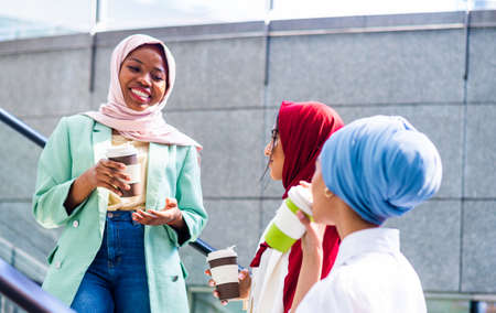 Multiethnic group of muslim girls wearing casual clothes and traditional hijab bonding and having...