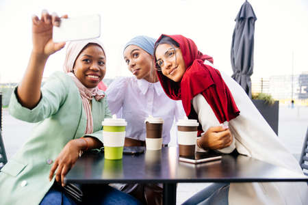 Multiethnic group of muslim girls wearing casual clothes and traditional hijab bonding and having fun outdoors - 3 arabic young girlsの写真素材