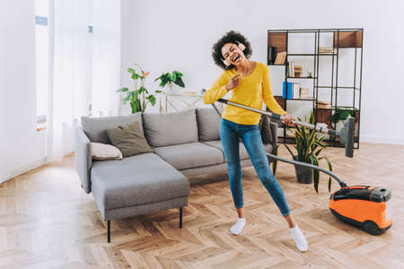 Happy woman cleaning home with vacuum cleaner and listening music - Housewife doing her homeworks, domestic life sceneの写真素材