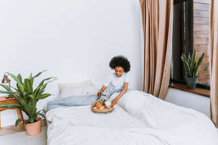 Afro-american girl resting in bed at home - Beautiful woman relaxing at home having breakfast in bed