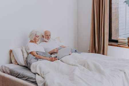 Beautiful senior couple enjoying time together at home - Moder elderly couple surfing the internet on laptop computerの写真素材