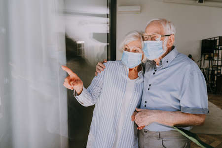 Elderly couple with protective face masks at home during covid-19 pandemic quarantine - Old people in quarantine respection social distance and isolation on coronavirus virus spreadの写真素材