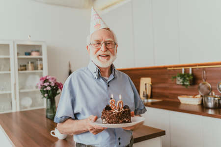Beautiful senior couple celebrating anniversary with birthday cake - Elderly couple having birthday party at homeの写真素材