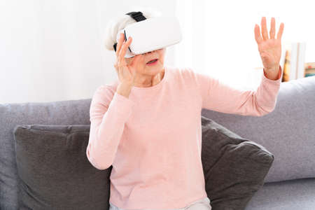 Beautiful elderly woman with vr googles at home - Mature woman playing with virtual reality worldの写真素材