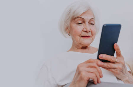Beautiful senior woman checking social network app on cellphone before going to sleep