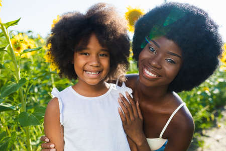 Beautiful afro-american mom and daughter palying and having fun in a sunflowers fieldの写真素材