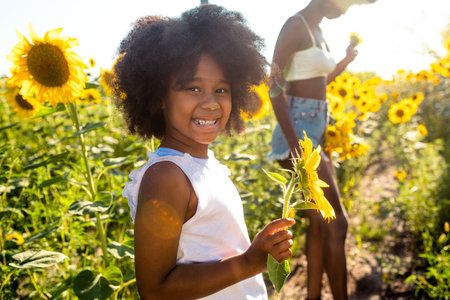 Beautiful afro-american mom and daughter palying and having fun in a sunflowers fieldの写真素材
