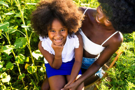 Beautiful afro-american mom and daughter palying and having fun in a sunflowers fieldの写真素材