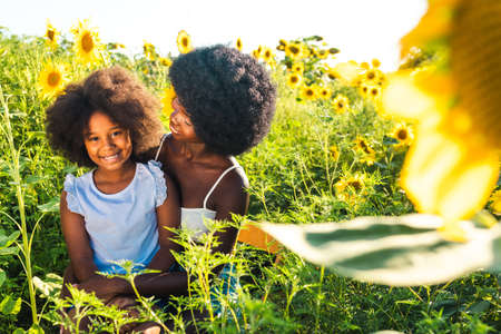 Beautiful afro-american mom and daughter palying and having fun in a sunflowers fieldの写真素材