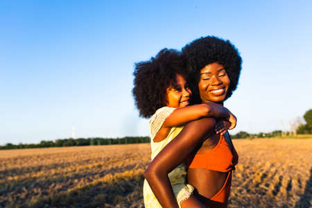 Beautiful afro-american mom and daughter palying and having fun in a sunflowers fieldの写真素材