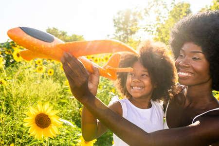 Beautiful afro-american mom and daughter palying and having fun in a sunflowers fieldの写真素材