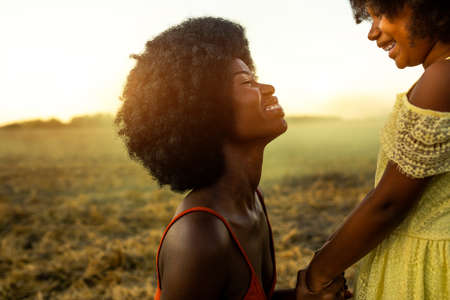 Beautiful afro-american mom and daughter palying and having fun in a sunflowers fieldの写真素材