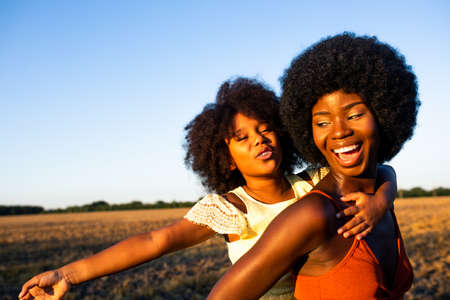 Beautiful afro-american mom and daughter palying and having fun in a sunflowers field